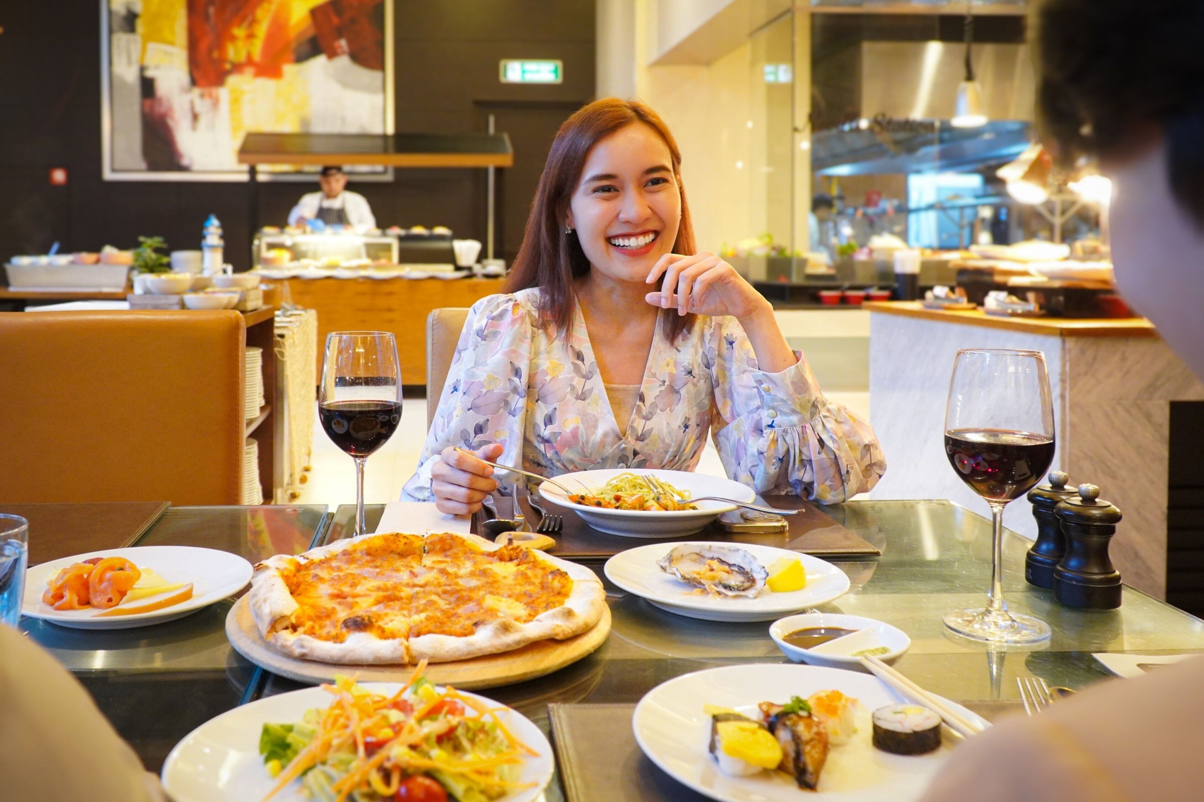 A dining area with a pizza, salad, and sushi on plates, along with wine glasses.