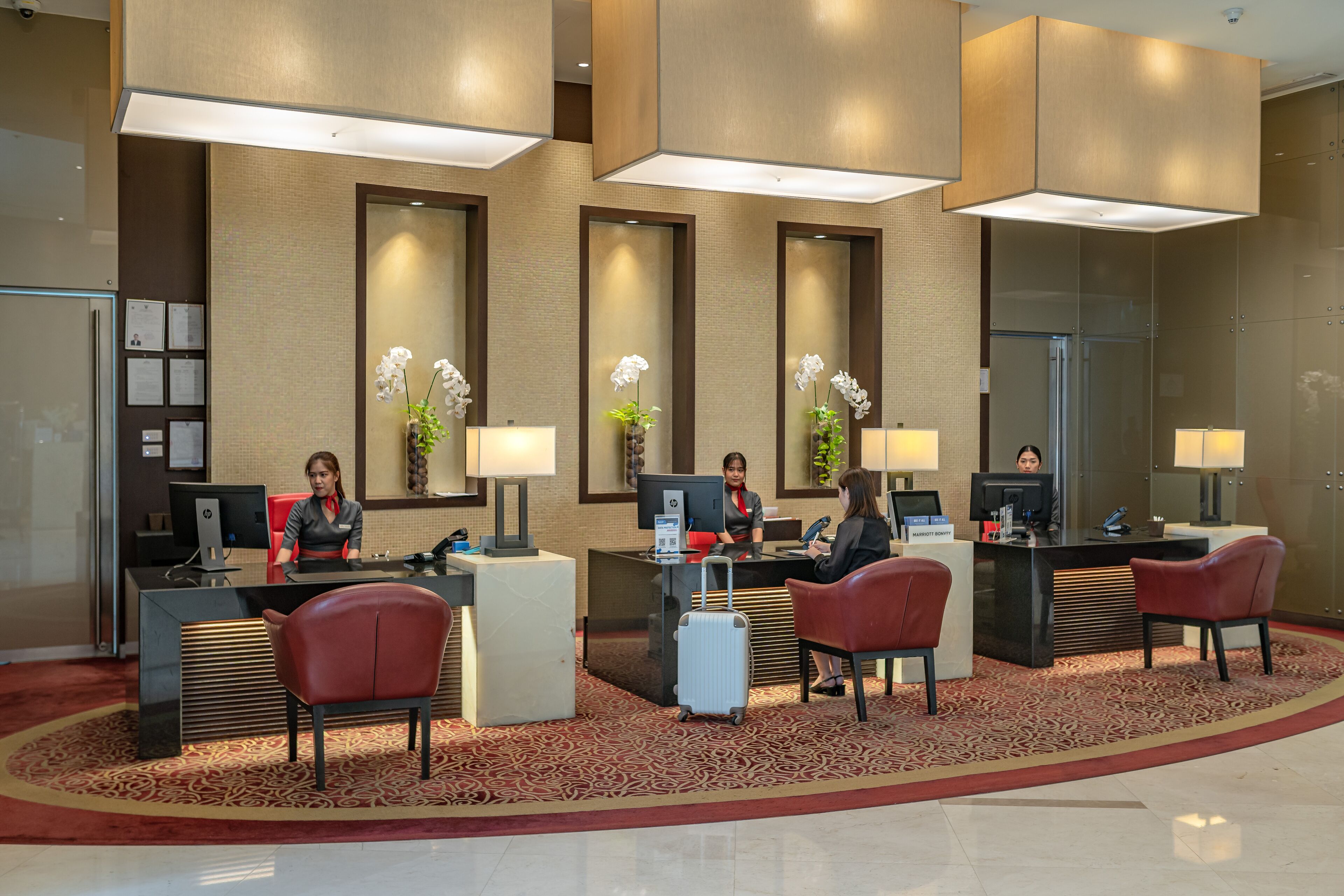 A hotel reception area with a modern design, featuring a reception desk, computers, and seating for guests.