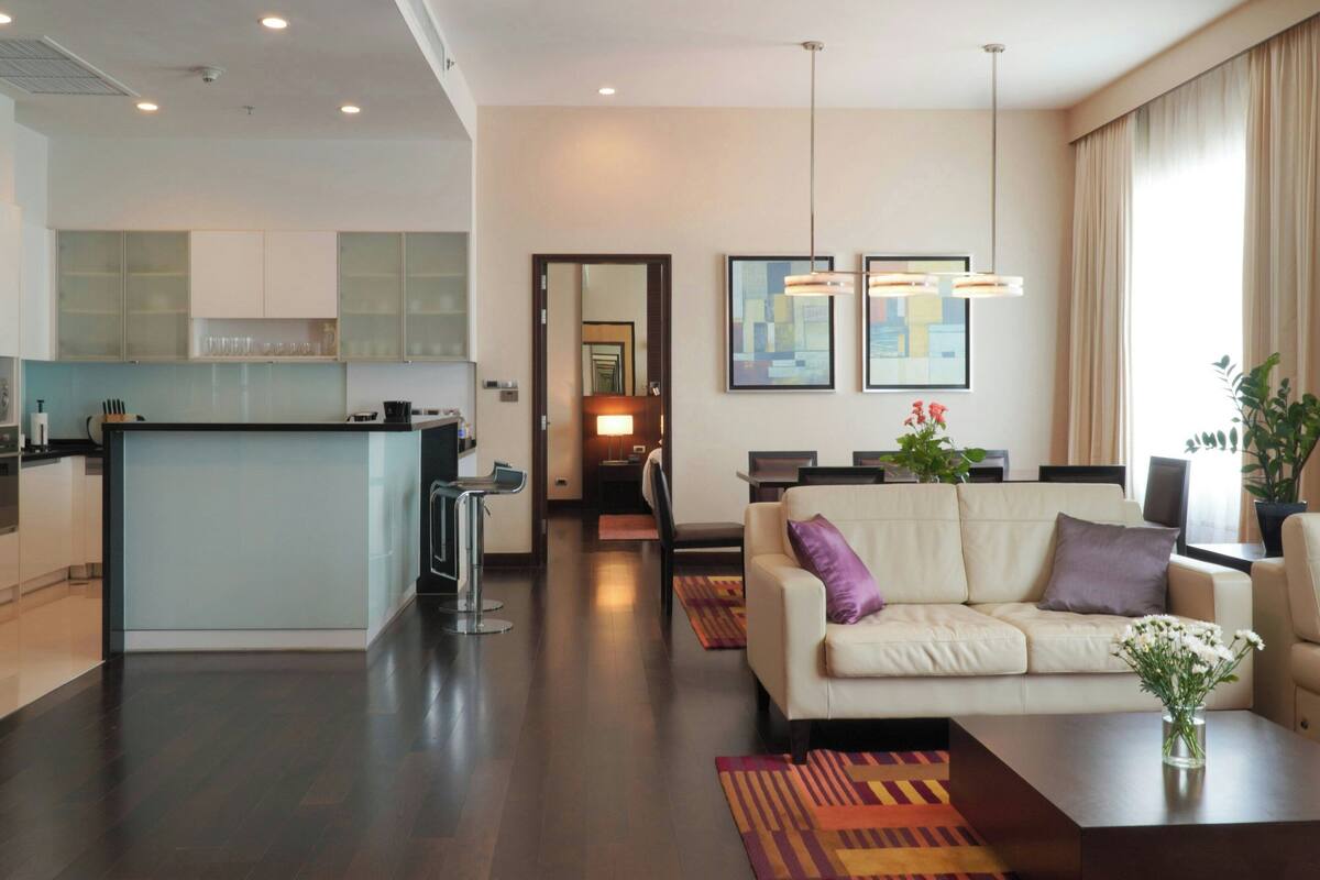 A modern kitchen with a central island, a dining area with a sofa and chairs, and a living room with a coffee table and a vase of flowers.