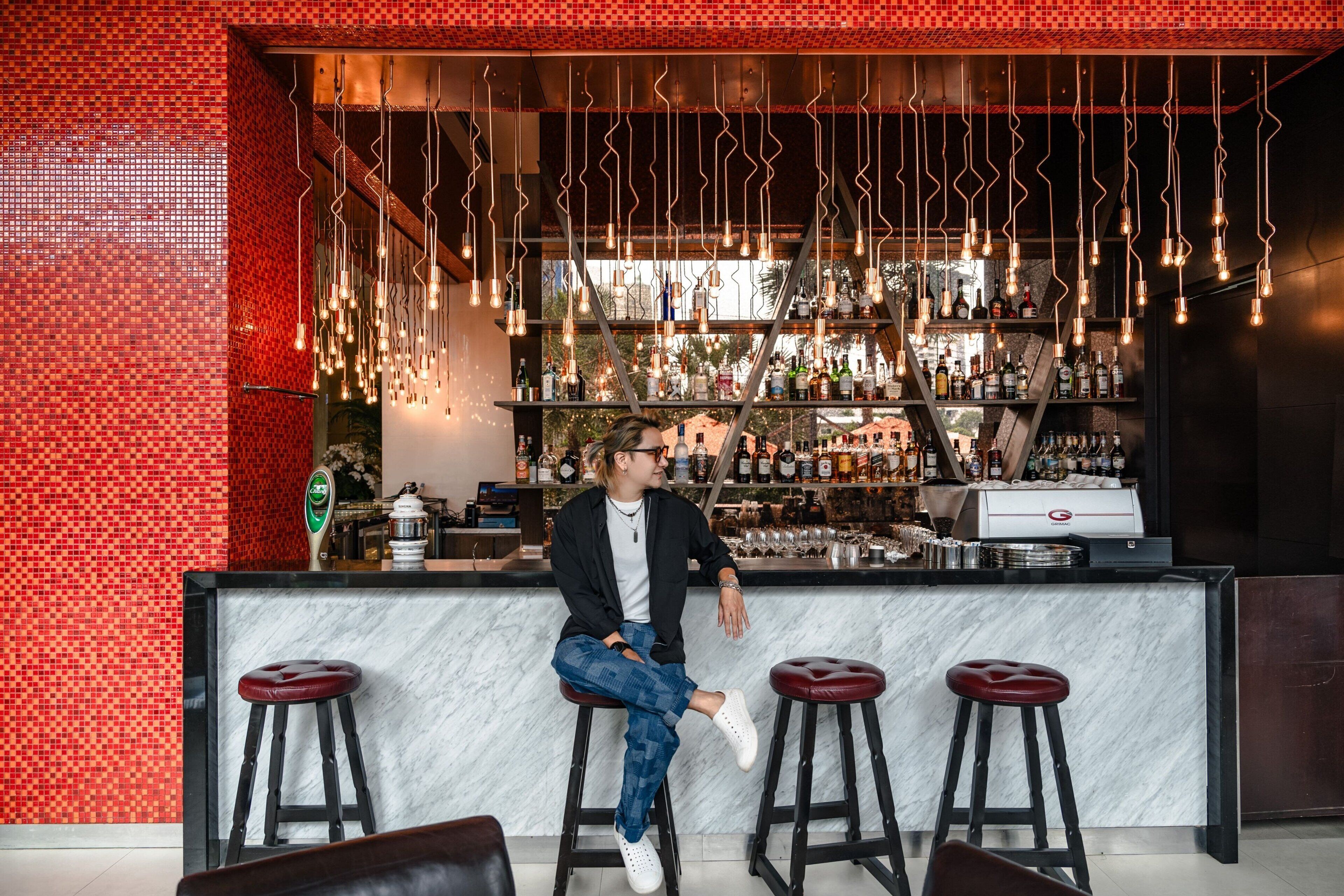 A bar area with a person sitting on a stool, a marble counter, and a red-tiled wall.