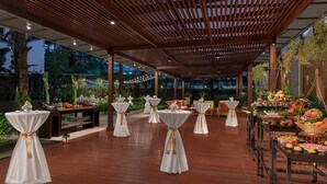 An outdoor dining area with wooden flooring, tables with white tablecloths and gold sashes, and a variety of food and drink displays. - Marriott Executive Apartments Sukhumvit Park, Bangkok (Bangkok)