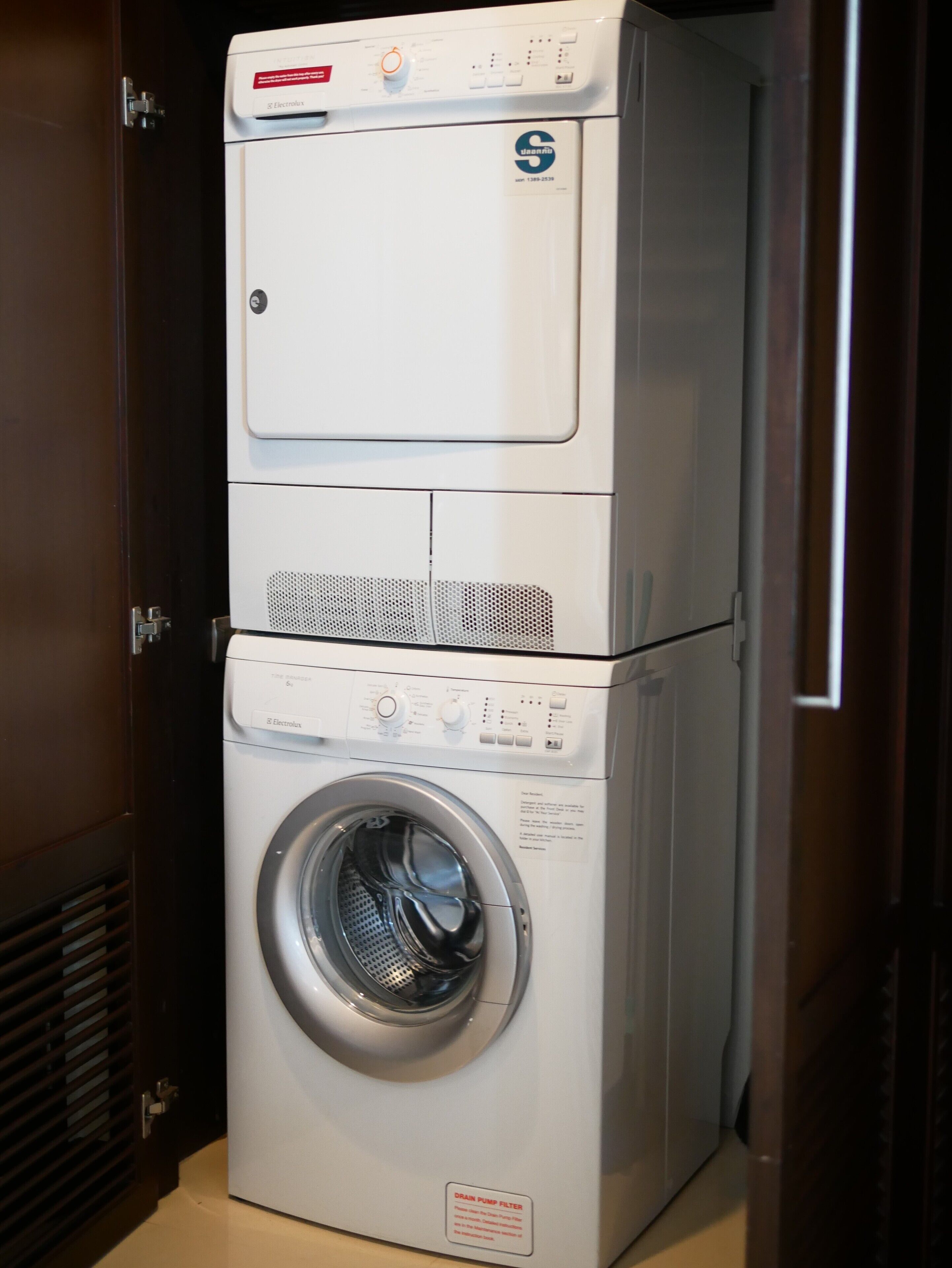 A stacked washer and dryer unit in a room with a wooden door and vent.