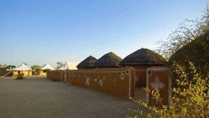 Une rangée de huttes traditionnelles aux toits de chaume, un sol sablonneux et un ciel dégagé.