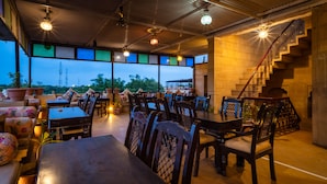 An indoor dining area with tables and chairs, large windows, and a staircase. - Hotel Fifu (Jaisalmer)
