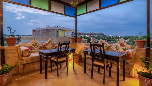 A terrace with a wooden table and chairs, a sofa with floral cushions, and potted plants. - Hotel Fifu (Jaisalmer)