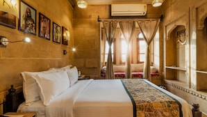 A well-lit room with a large bed, a nightstand, and a wall-mounted lamp. - Hotel Fifu (Jaisalmer)