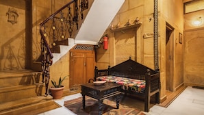 A traditional room with a wooden bed, a small table, a potted plant, and a staircase with a wrought iron railing. - Hotel Fifu (Jaisalmer)