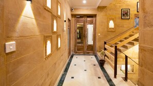 Un corridoio con pavimento in marmo, porte in legno e una scala con ringhiera in legno.