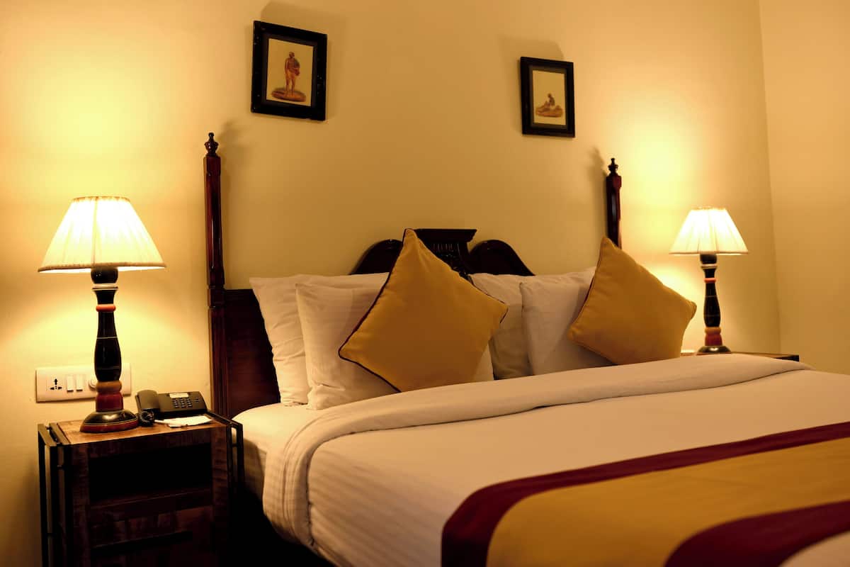 A hotel room with a bed, two bedside lamps, a nightstand with a phone, and two framed pictures on the wall.