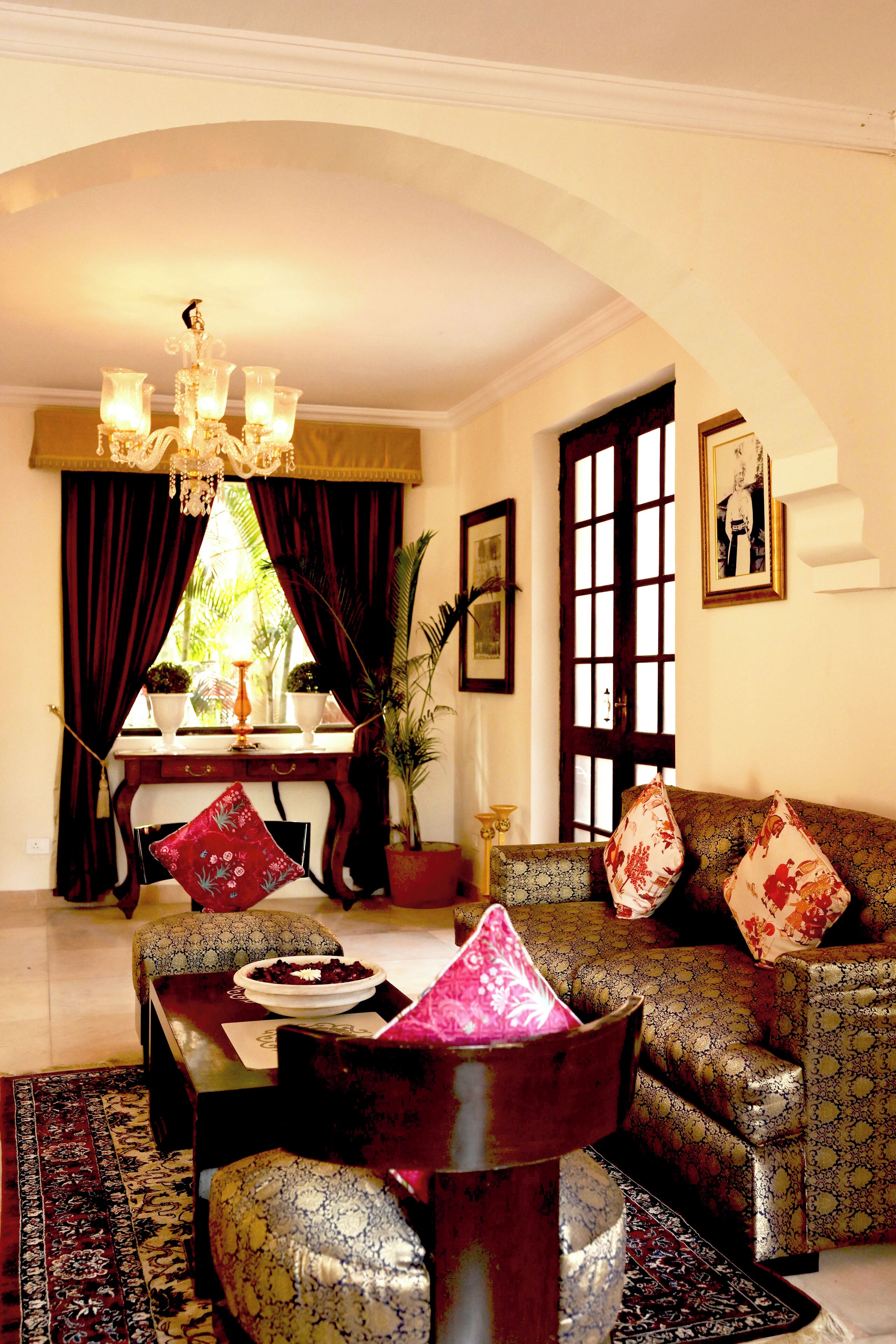 A living room with a sofa, a table, a chandelier, and a window with curtains.