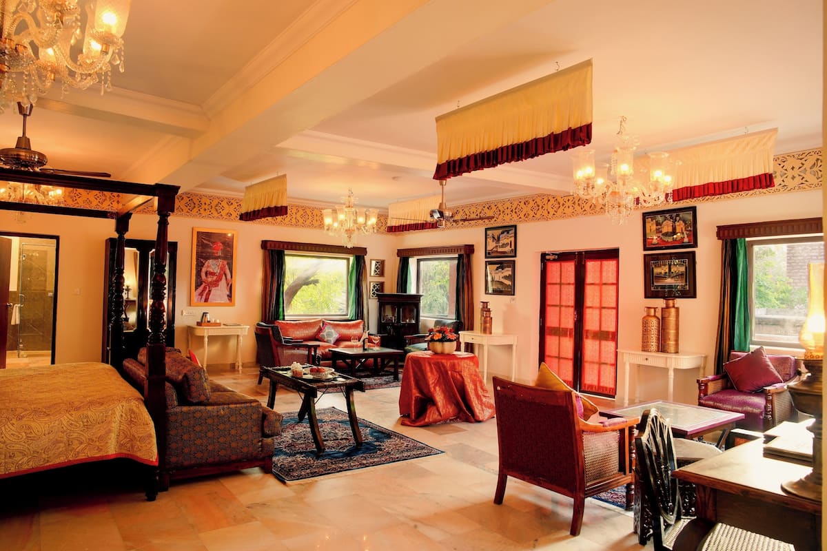 A spacious room with a four-poster bed, a sitting area with a sofa and armchairs, a dining table, and a chandelier.