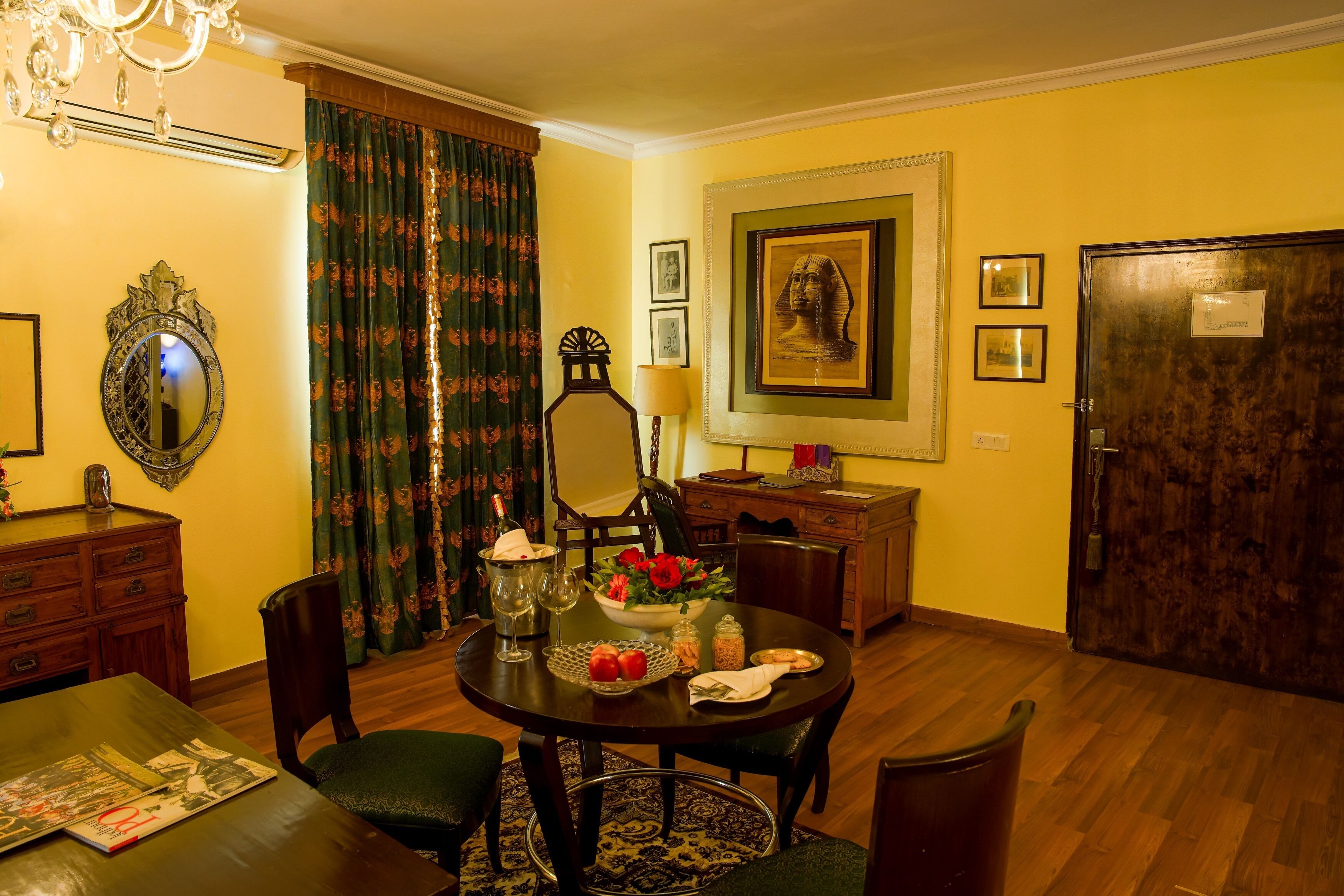 A dining room with a round table, chairs, a chandelier, a mirror, and a door.