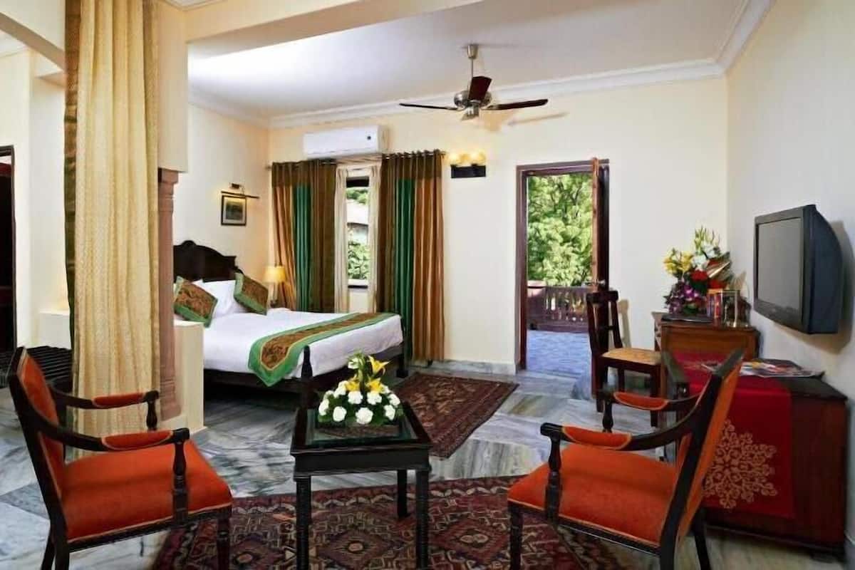 A hotel room with a bed, two chairs, a small table, a TV, and a balcony with a view.