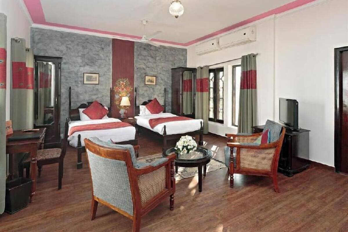 A hotel room with two beds, a sitting area with chairs, a small table, a television, and a ceiling fan.