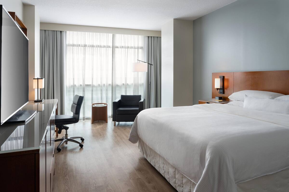 A hotel room with a large bed, a desk with a chair, a TV, and a window with curtains.