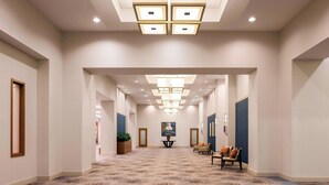 Passadís d'hotel amb un terra estampat, il·luminació encastrada i una zona de seients amb cadires i taula.