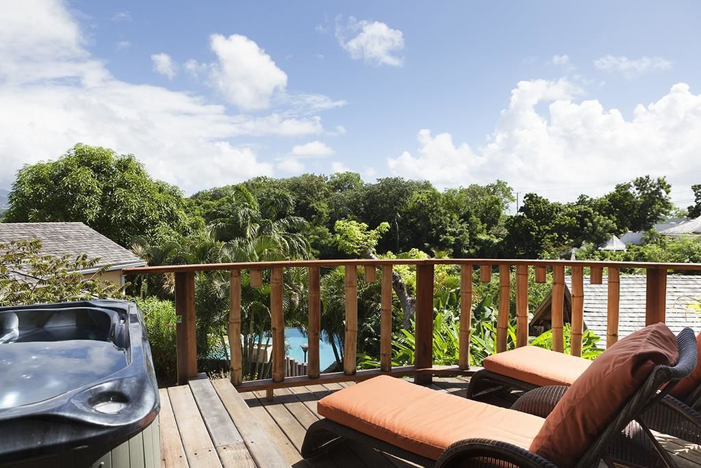 Una terraza de madera con un jacuzzi, sillones de descanso y vistas a una piscina y abundante vegetación.