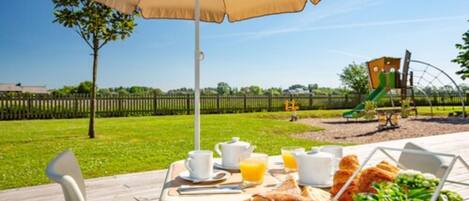 Disposição para café da manhã ao ar livre, com mesa, cadeiras e um grande guarda-sol.