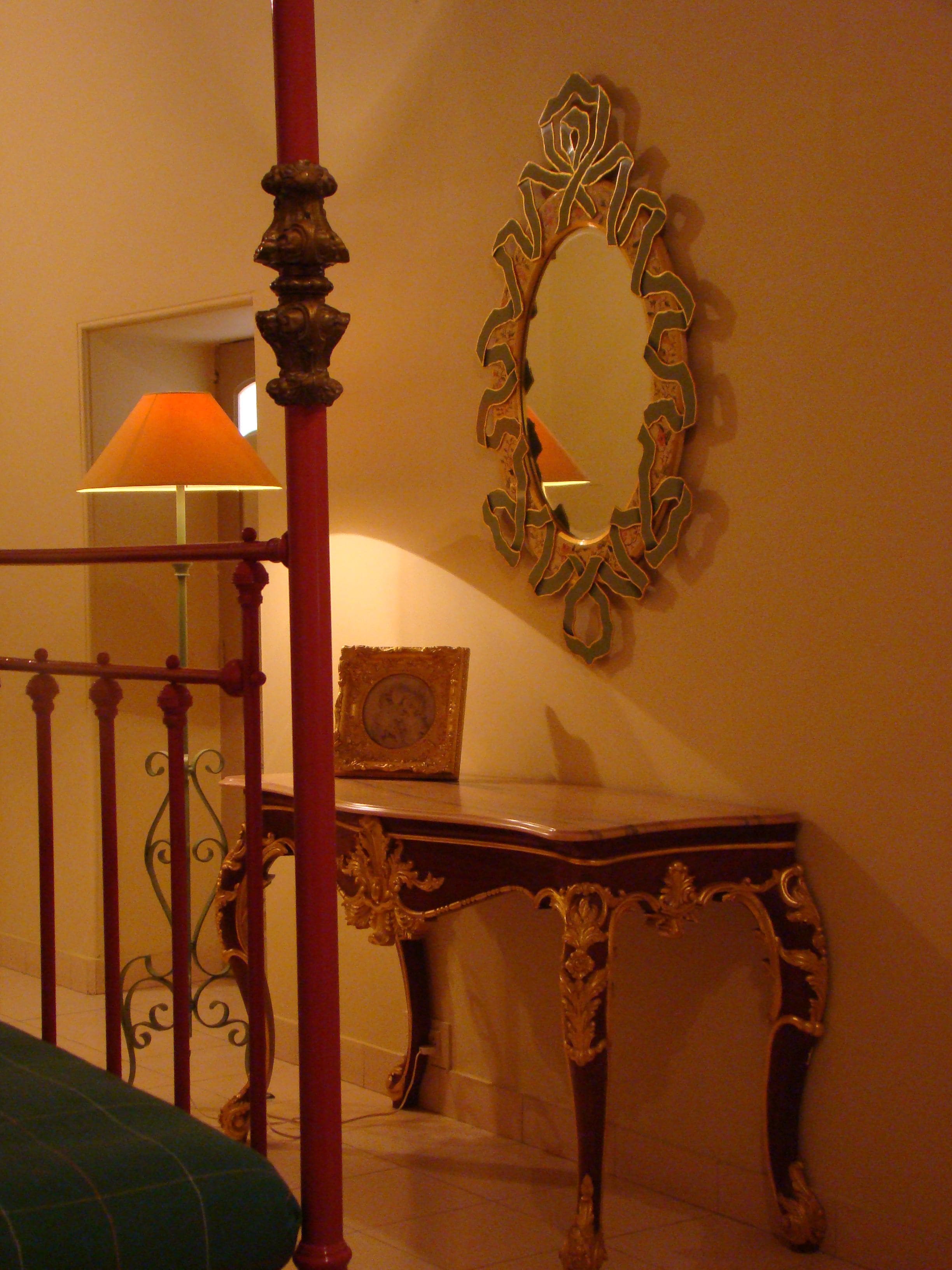 A room with a four-poster bed, a mirror with ornate frame, and a lamp on a table.