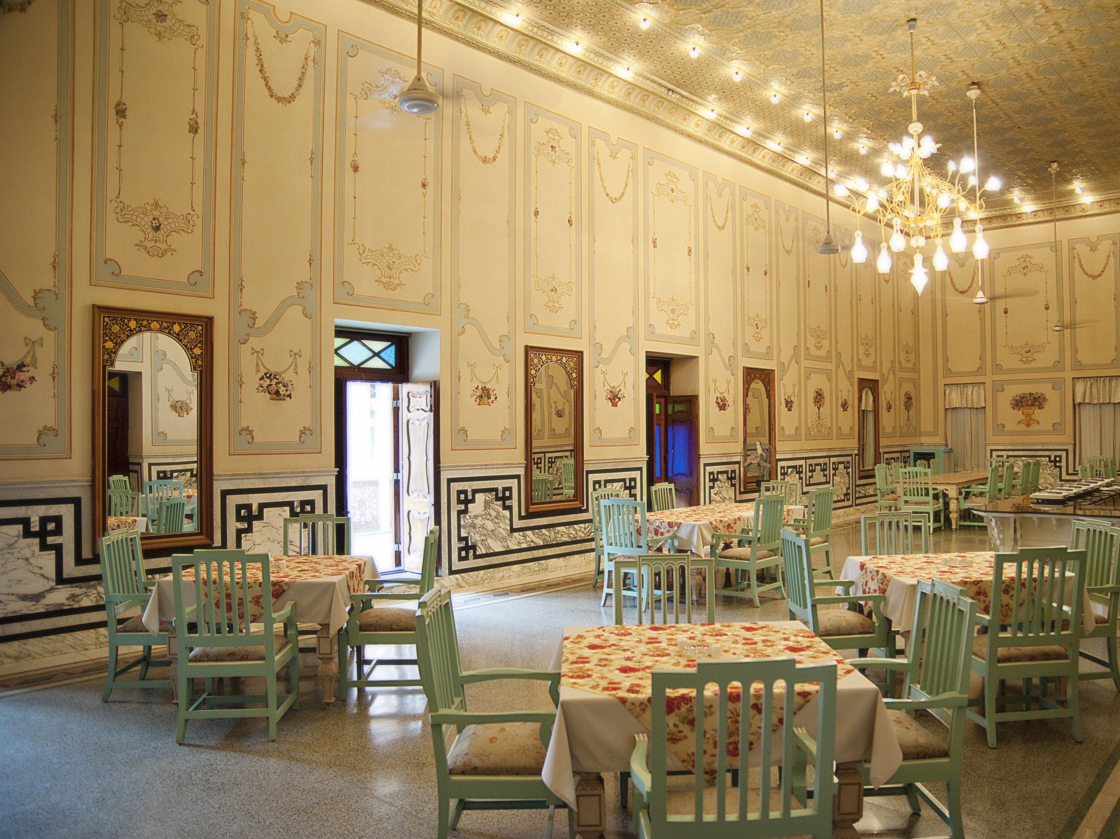 A spacious dining hall with ornate wall decorations, green chairs, and tables set for dining.