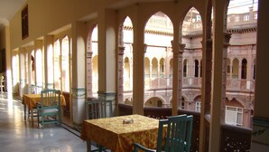 Un comedor con mesas y sillas, ventanas arqueadas grandes y vistas a un edificio con arquitectura detallada.