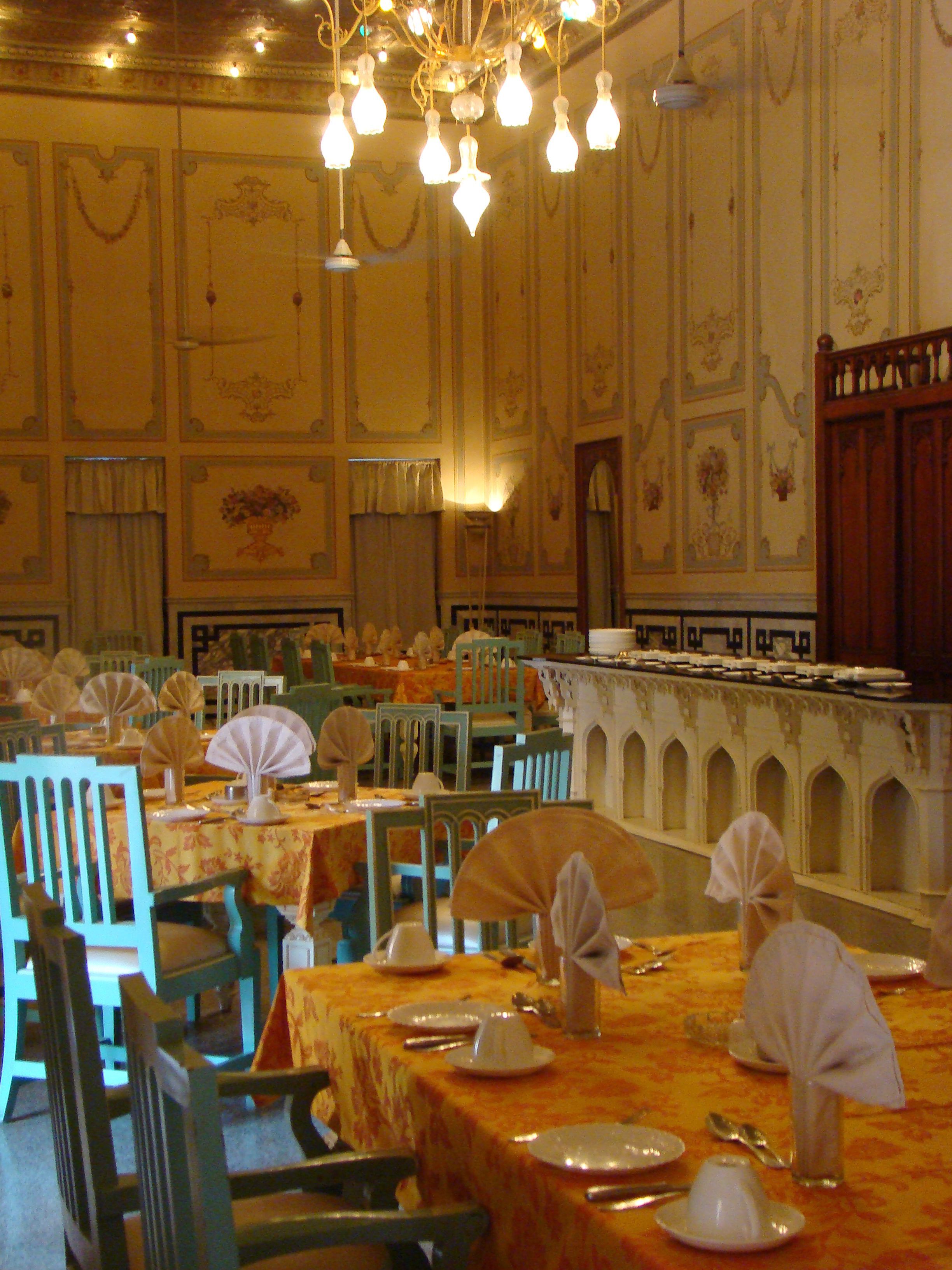 Una sala de banquetes amb taules preparades per dinar, cadires i una barra llarga amb una barana decorativa.