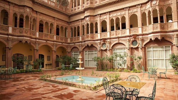 Un patio con piscina, mobiliario y arquitectura ornamentada.