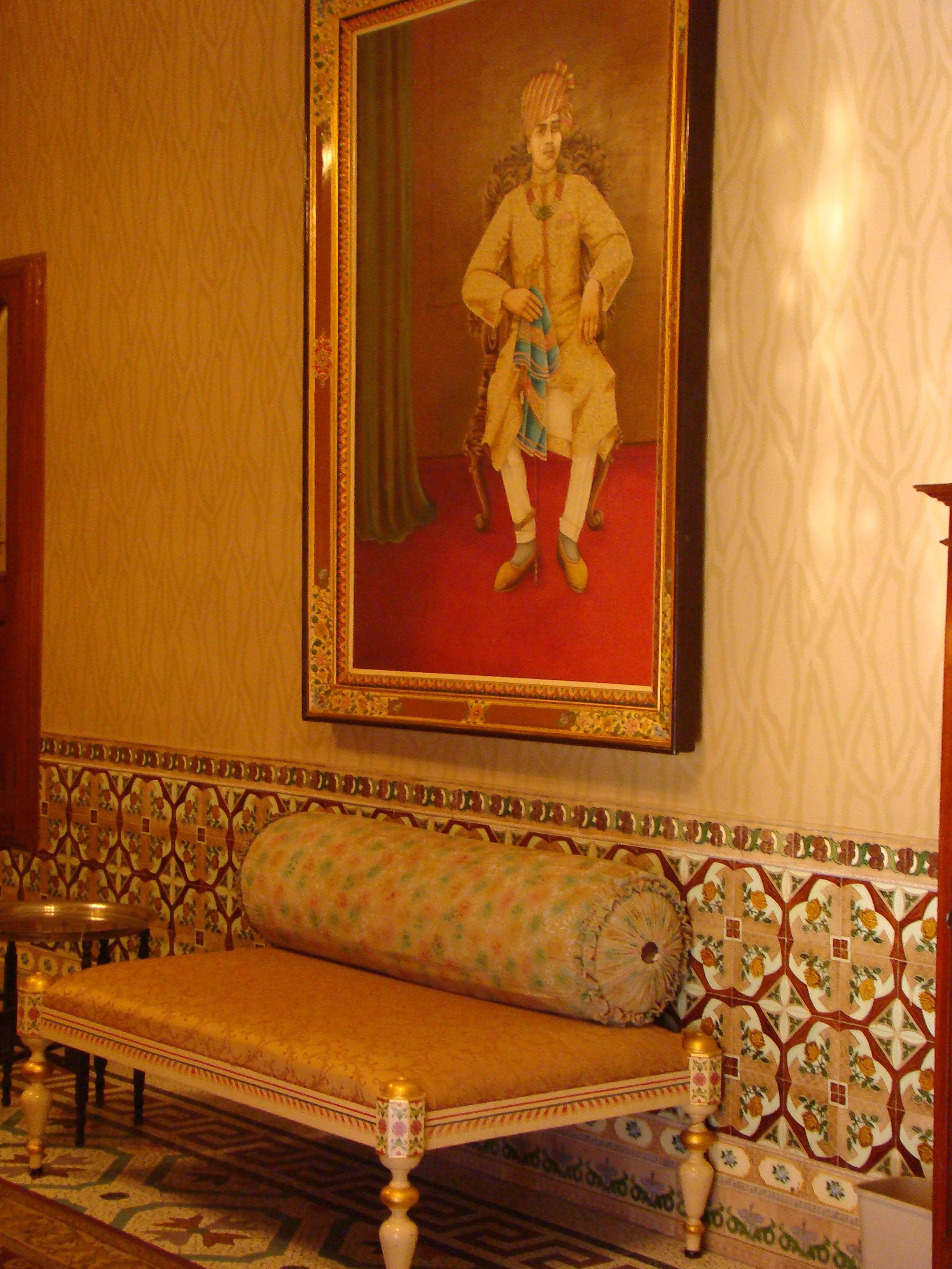 A room with a patterned bench, a framed portrait on the wall, and a tiled floor.
