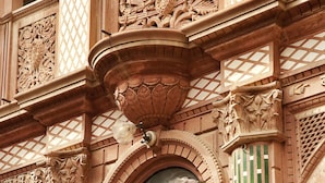 Fachada de edificio con intrincados relieves, una ventana circular y lámparas decorativas.