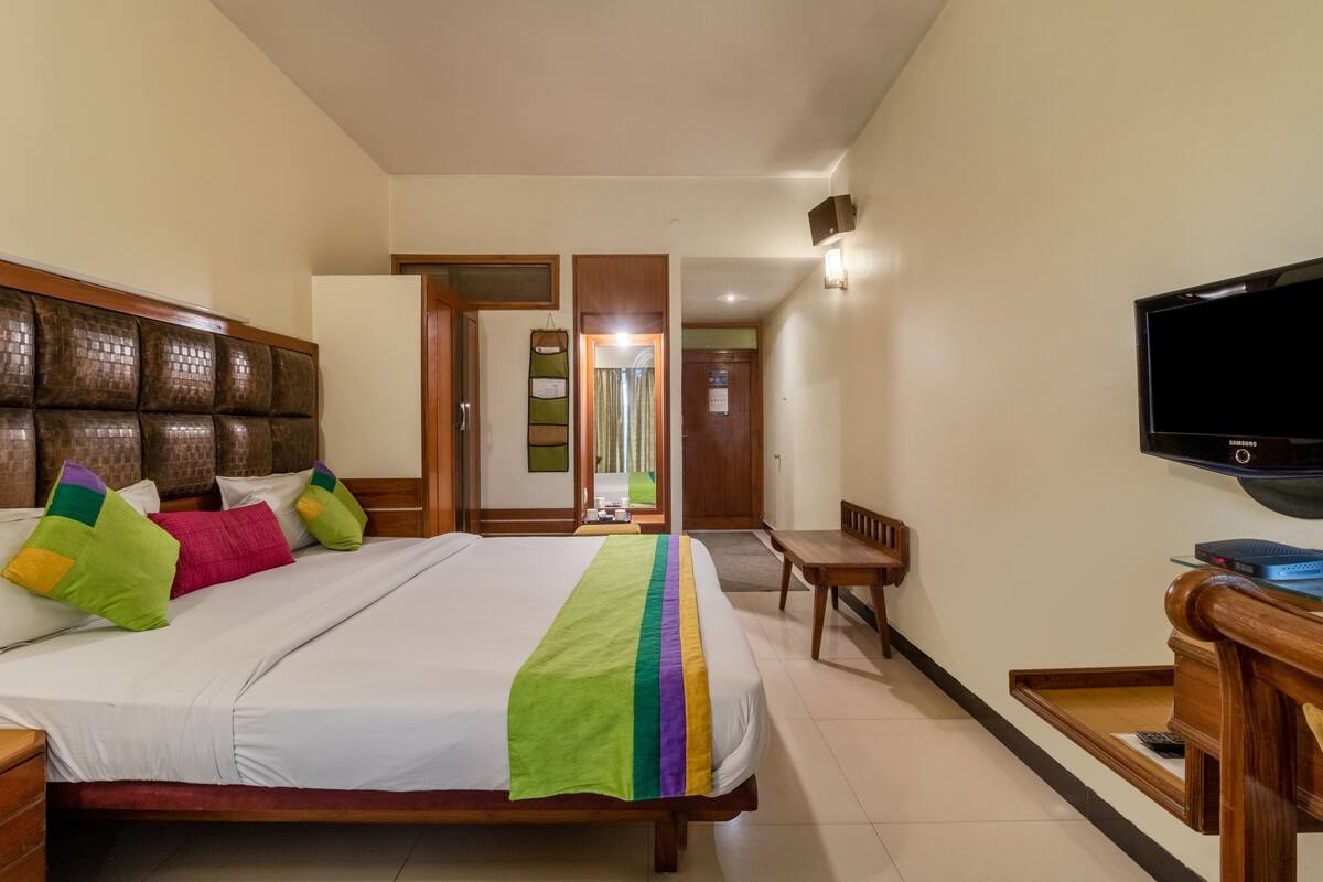 Una habitación de hotel con una cama grande, televisión, escritorio de madera y espejo.