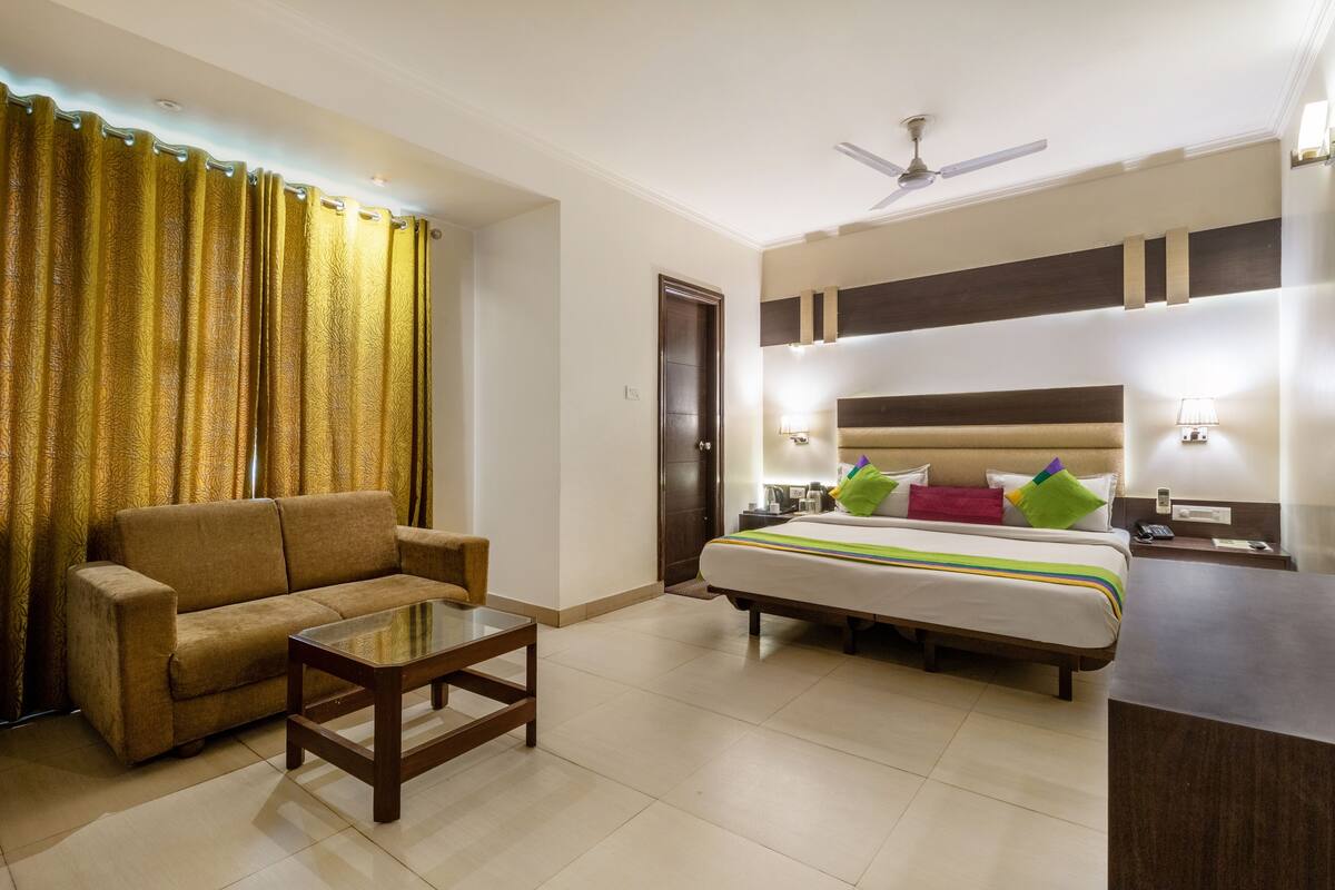 Habitación de hotel con sofá, cama con almohadas, mesita de noche, mesa y ventilador de techo.