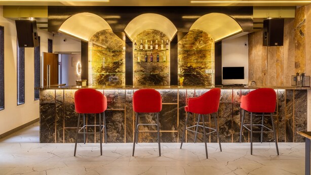 A bar area with three red bar stools, a marble countertop, and a television screen. - Treebo Natraj - Jaipur (Jaipur)