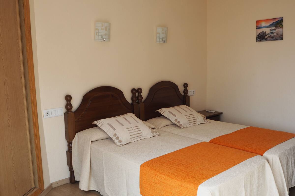 A double bed with two pillows, a nightstand, and a wall-mounted light fixture.