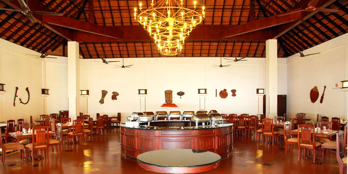 A spacious dining area with a central round table surrounded by chairs, a chandelier, and wall-mounted musical instruments.