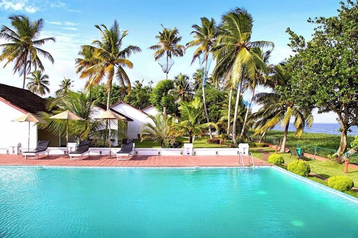 A pool area with lounge chairs, palm trees, and a view of the ocean.