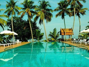 A pool with clear water, surrounded by palm trees and lounge chairs. - Abad Whispering Palms (Kottayam)