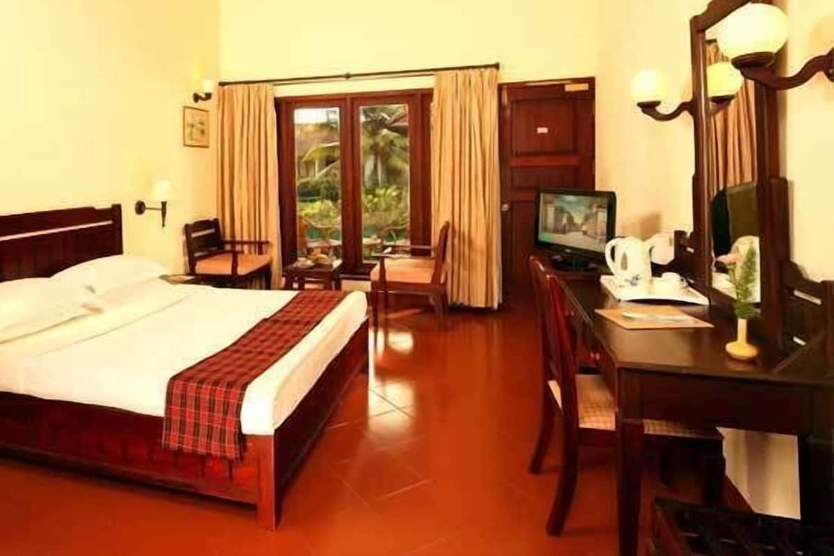 A hotel room with a bed, a desk with a computer, a TV, and a window with curtains.