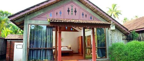 Una casa de un piso con un porche, una cama y una ventana con cortinas.