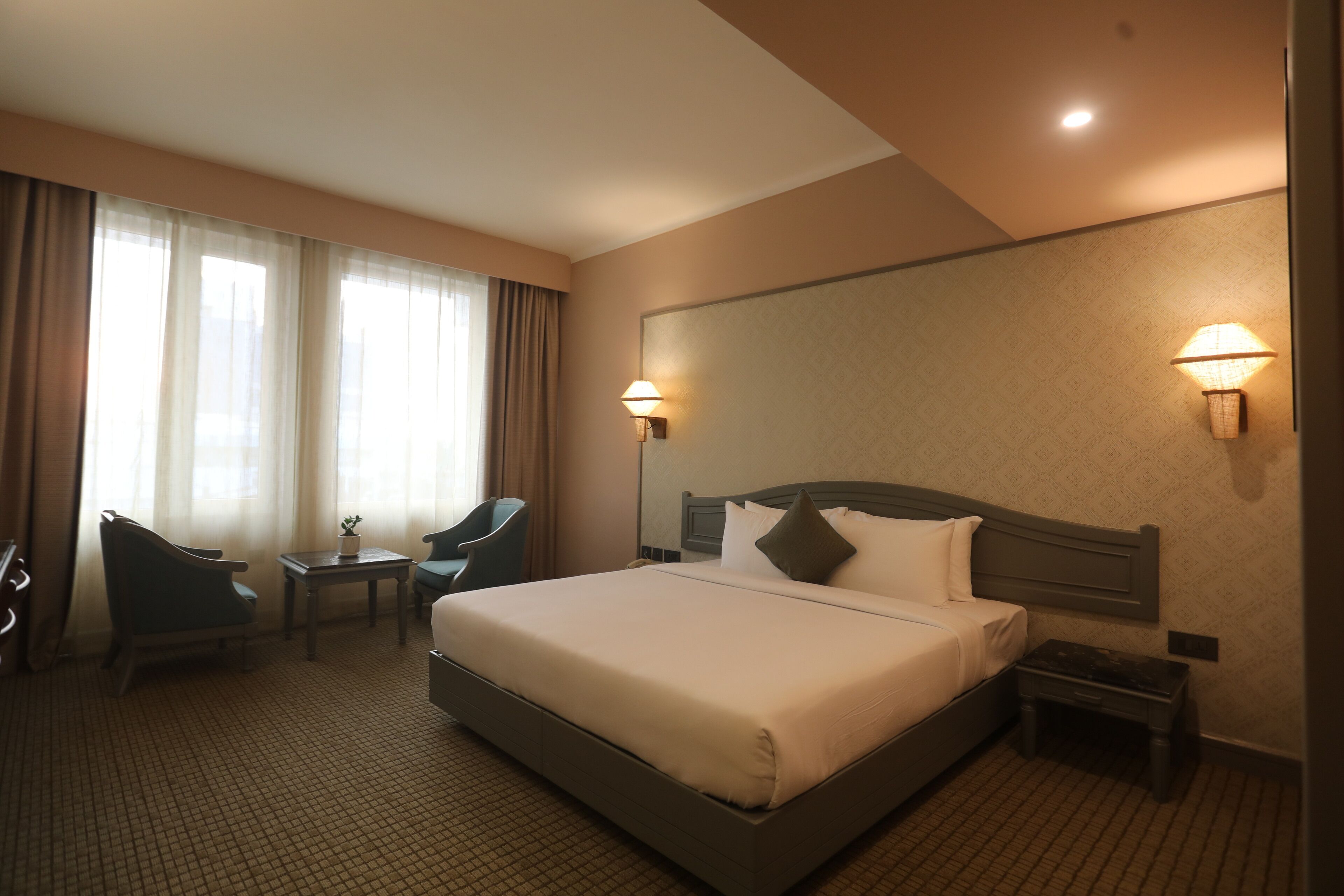 A hotel room with a large bed, two bedside tables, a chair, a small table, and a lamp.
