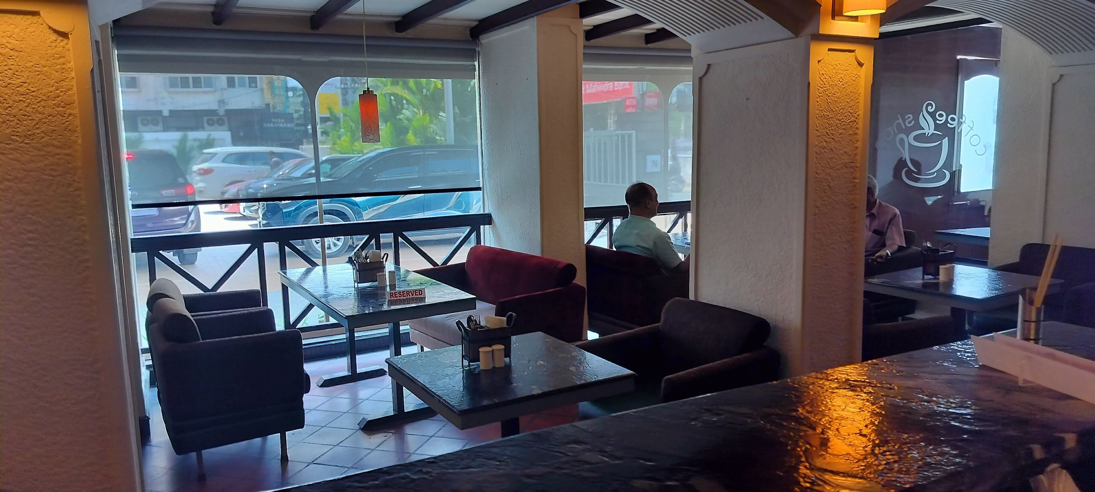 A restaurant with outdoor seating, a 'RESERVED' sign on a table, and a view of parked cars outside.
