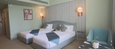 A hotel room with two beds, a small table, a chair, and a potted plant.