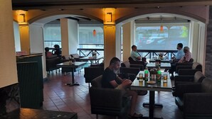 Restaurante com mesas ao ar livre, uma tela grande exibindo uma cena de estrada e alguns clientes.