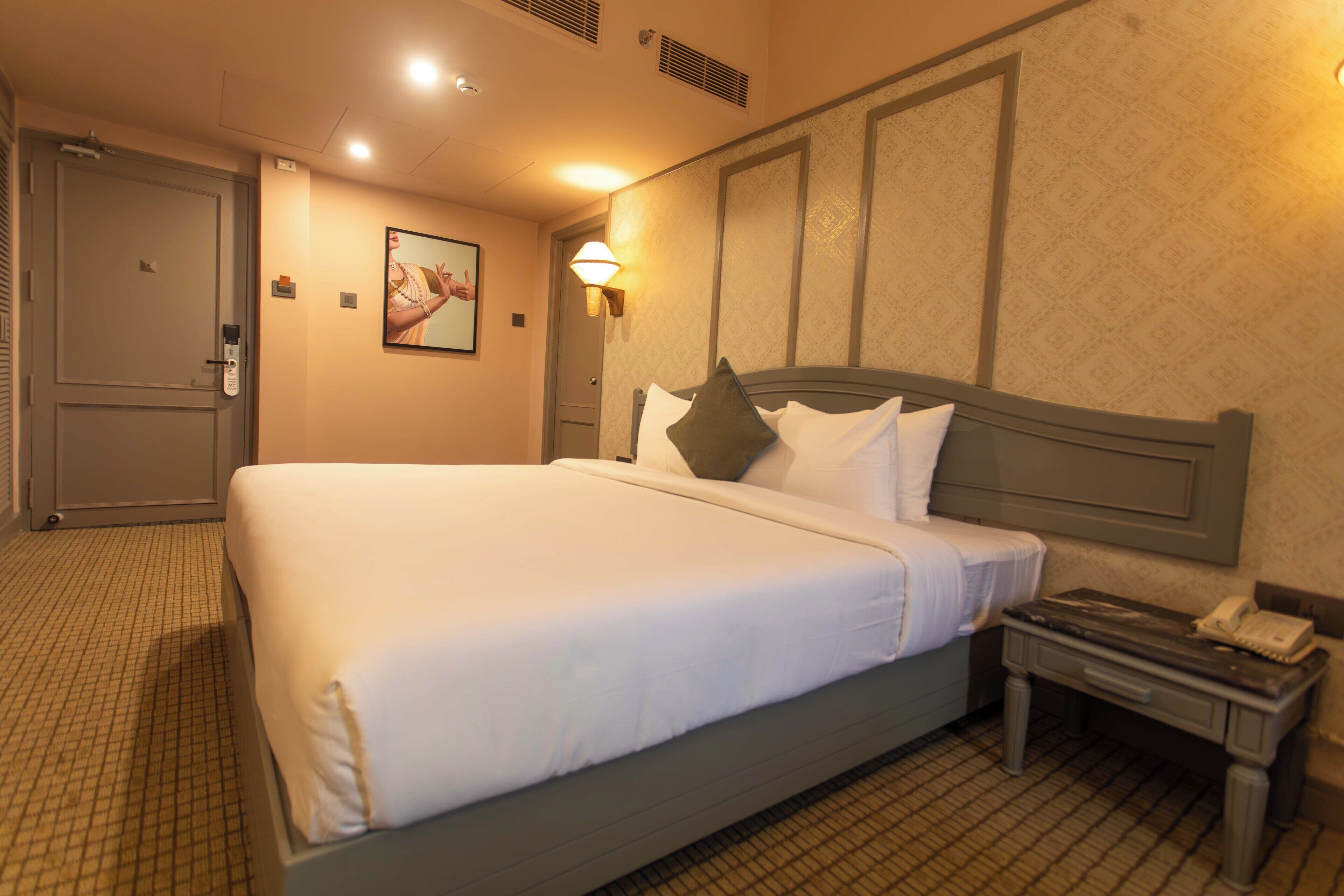 A hotel room with a large bed, a bedside table with a phone, and a wall-mounted lamp.