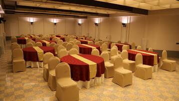 Un salón de conferencias con varias mesas redondas, cada una cubierta con un mantel rojo y amarillo, rodeado de sillas beige.