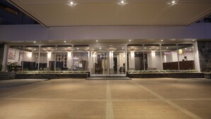 Entrada de hotel com fachada de vidro, balcão de recepção e área de estar.