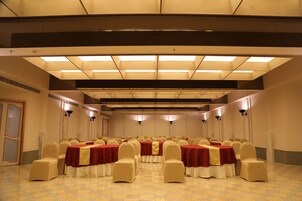 A conference room with rows of tables and chairs, equipped with ceiling lights and wall-mounted lamps.