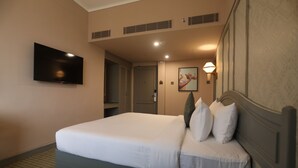 Quarto de hotel com uma cama grande, televisão de tela plana na parede, mesa de cabeceira e porta que dá para o banheiro.