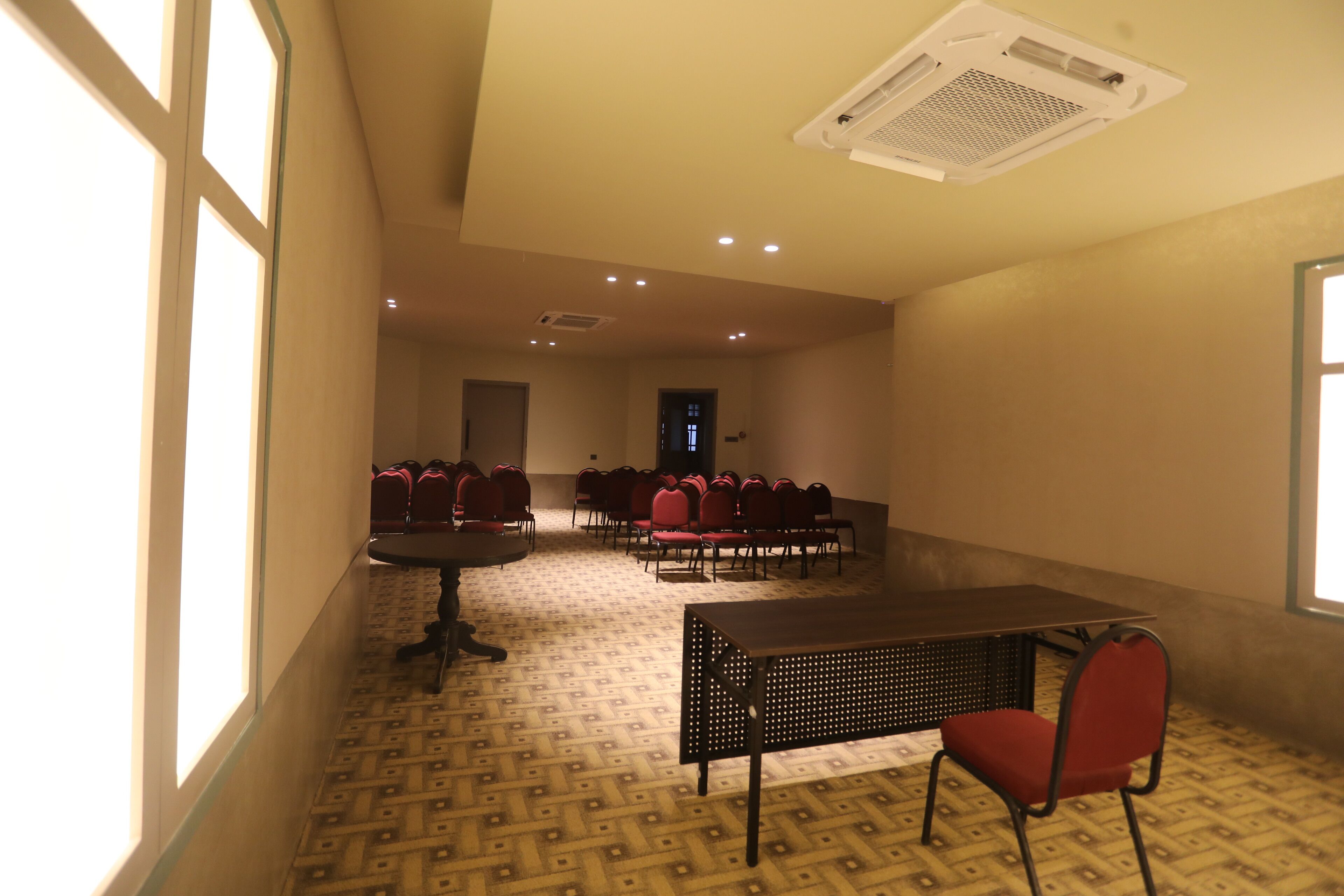 A conference room with tables and chairs, a patterned floor, and a ceiling vent.