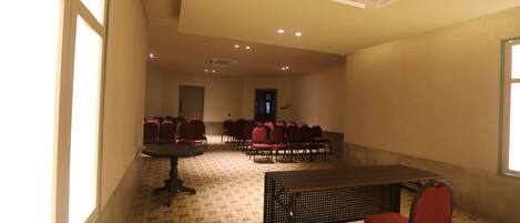 A conference room with tables and chairs, a patterned floor, and a ceiling vent.