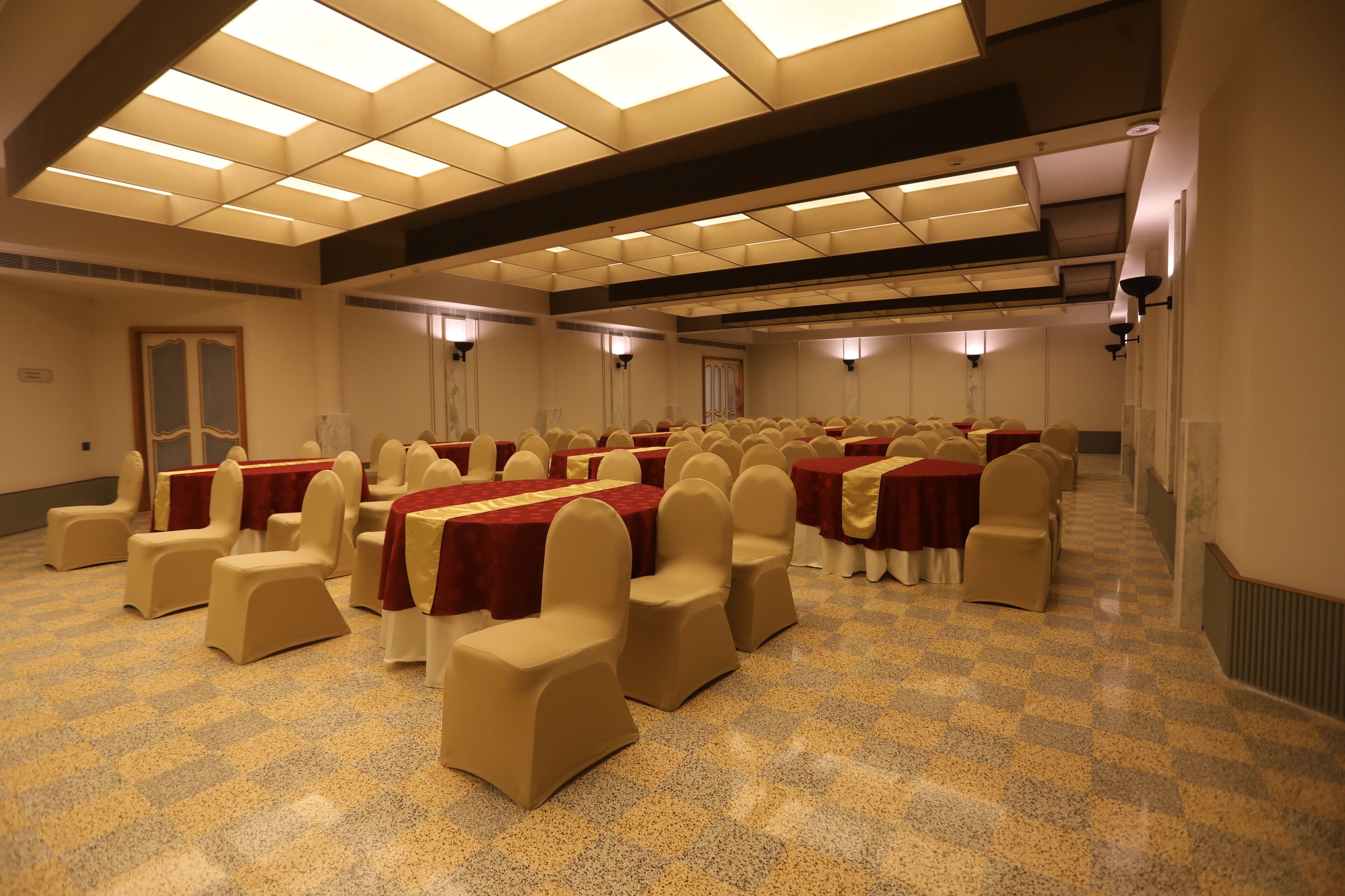 A conference room with rows of tables and chairs, equipped with overhead lighting and a checkered floor.